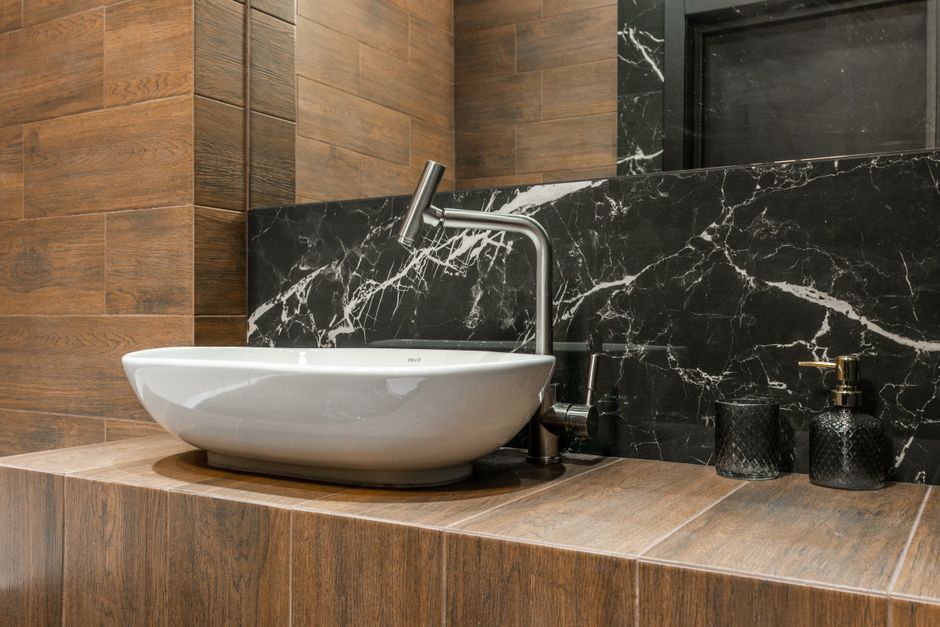 Detail of interior design of contemporary home bathroom with white sink and chrome tap on wood like tiled counter near wall with mirror and marble tiles